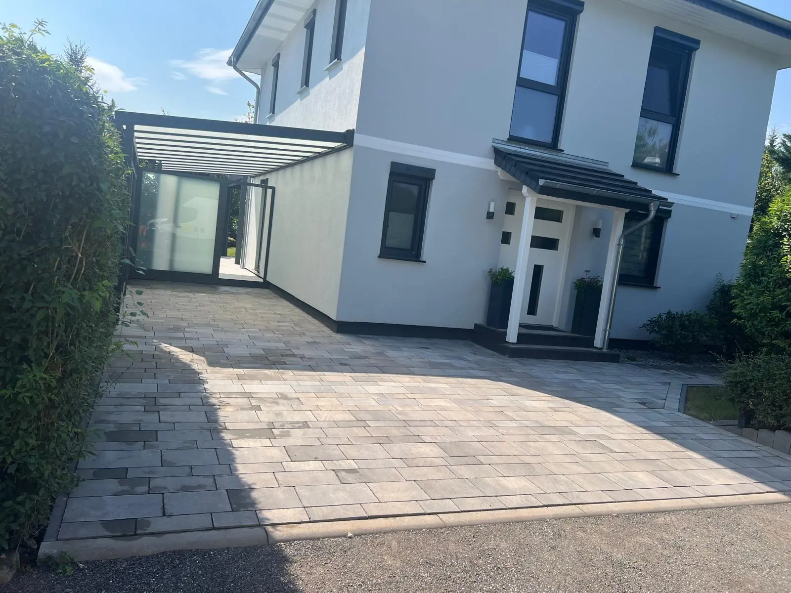 Gepflasterte Zufahrt vor dem Wohnhaus mit Carport und Hauseingang.